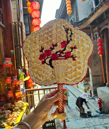 The bamboo woven fan has a plum blossom pattern on it.