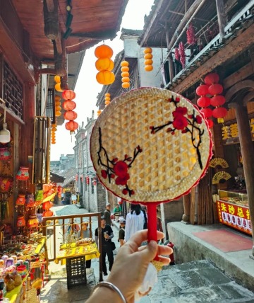 A tourist is showing off a bamboo woven fan they bought in Furong Town.