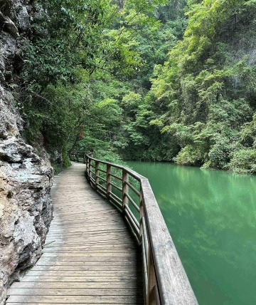 One side of the wooden boardwalk is the rocky wall of the valley, and the other side is the crystal-clear blue lake.