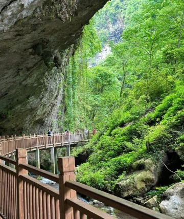 Above the wooden boardwalk is a rocky wall extending into mid-air, with hikers walking below.