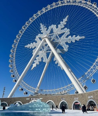 In the center of the ice Ferris wheel is a giant snowflake, with many tourists taking photos below.