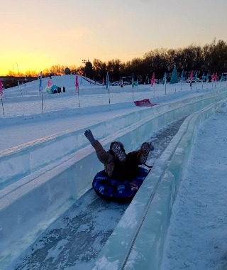 A tourist cheers as they slide down the super ice slide, visibly thrilled.