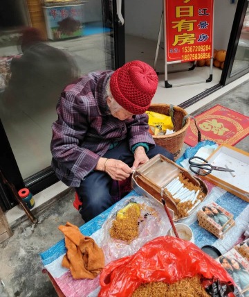 An elderly woman in Furong Ancient Town is making hand-rolled cigarettes.