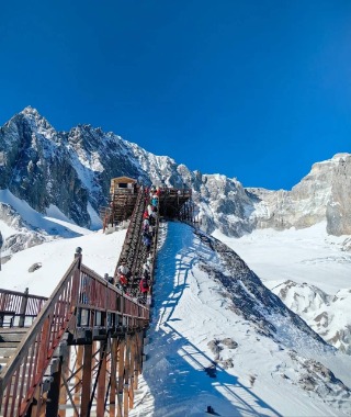 Tourists are trekking up Jade Dragon Snow Mountain on a wooden walkway.