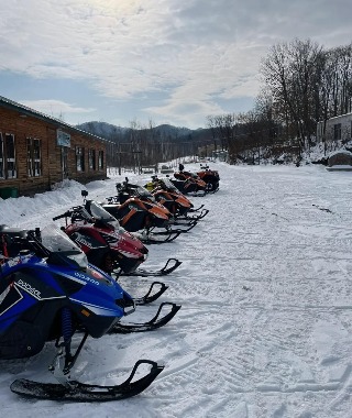 A row of snowmobiles is lined up on a snowy path.