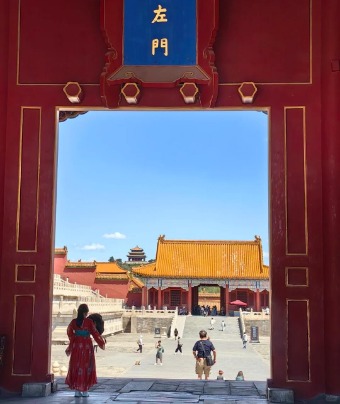 The tourists are walking through a red gate inside the Forbidden City.