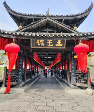 Tourists are exploring the Tuwang Bridge, which is lined with red lanterns on both sides.