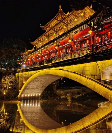 At night, the Tuwang Bridge lights up with a warm yellow glow.