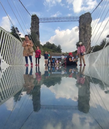 The surface of the Glass Bridge China Zhangjiajie reflects the sky and the tourists standing on it.